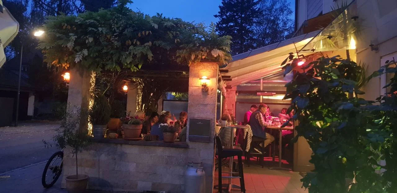 Ein Restaurant bei Abenddämmerung mit Gästen im Freien unter Pflanzenbeleuchtung.